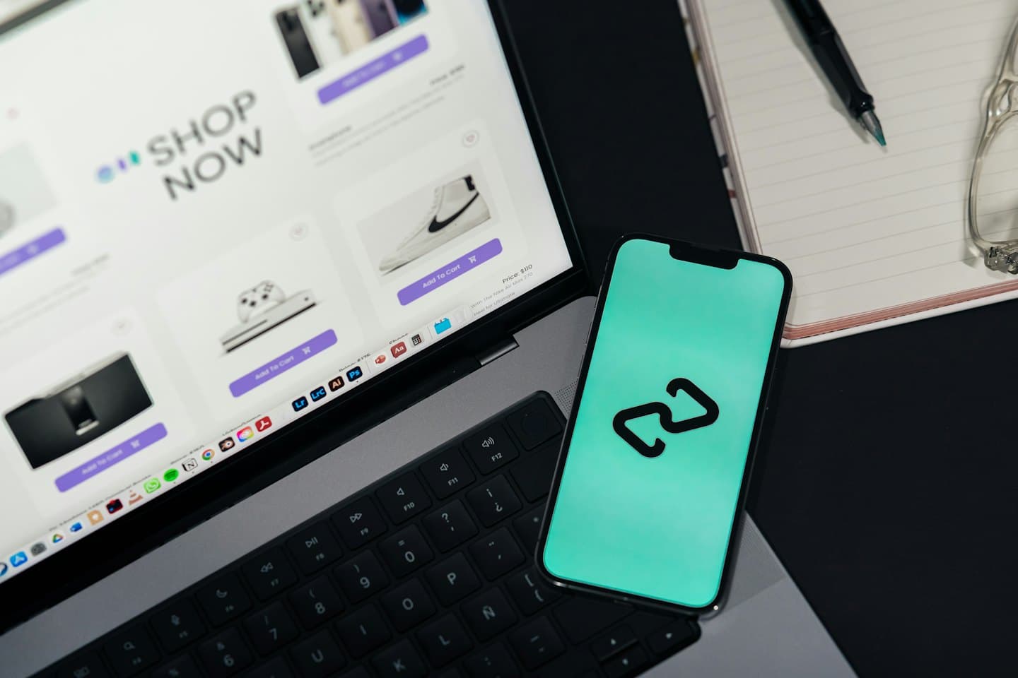 Masa üzerinde dizüstü bilgisayar, akıllı telefon, not defteri ve kalem.